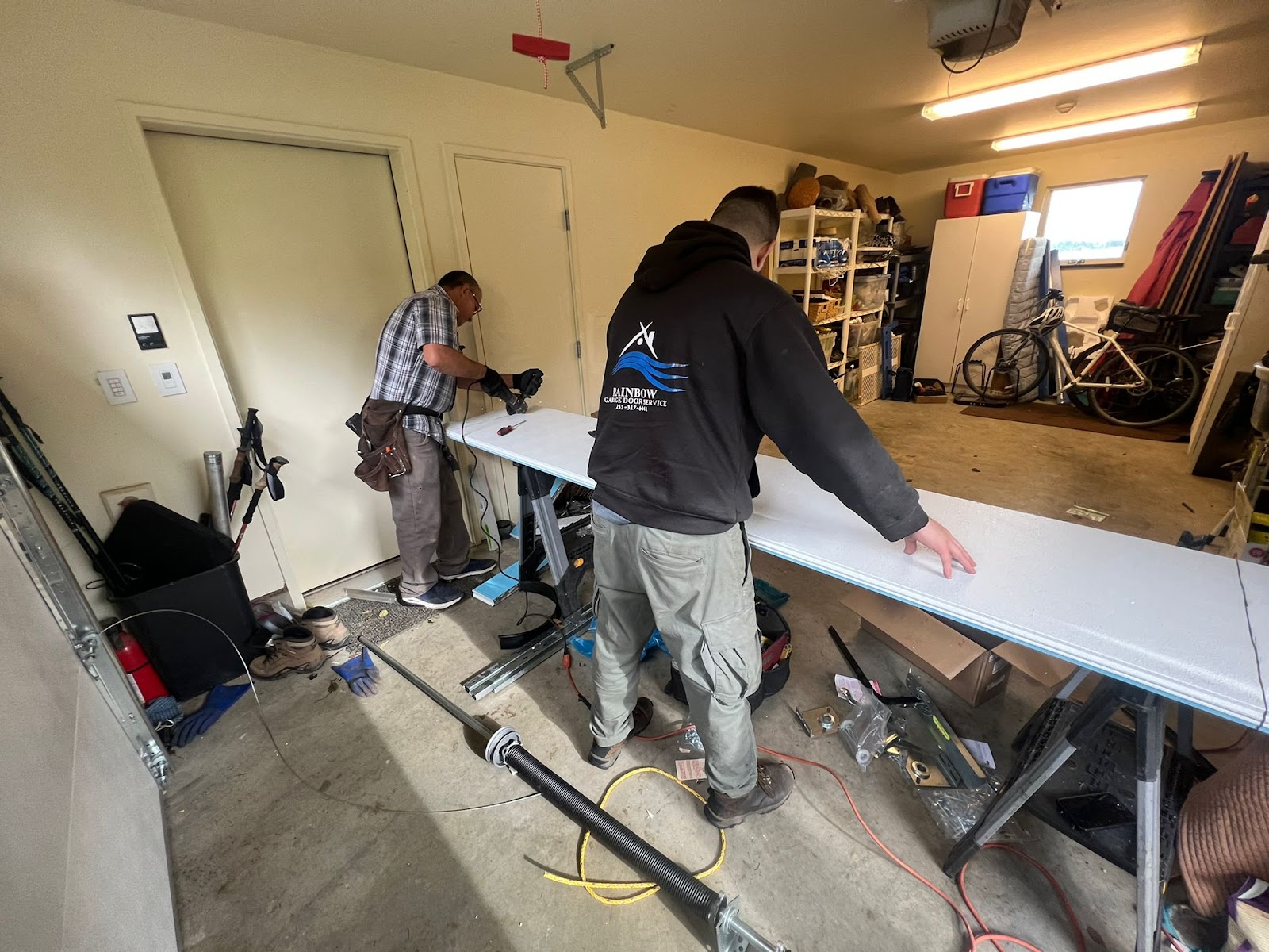 Two Rainbow Garage Door technicians working on a garage door panel in a residential garage