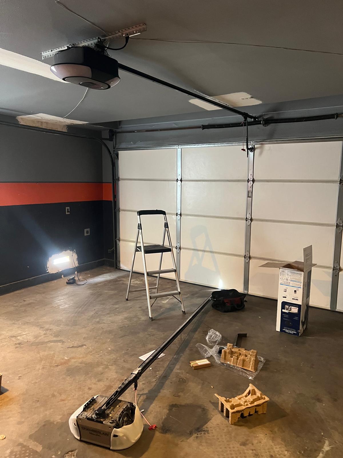 Garage door opener installation in progress with ladder, rail and old opener on the floor