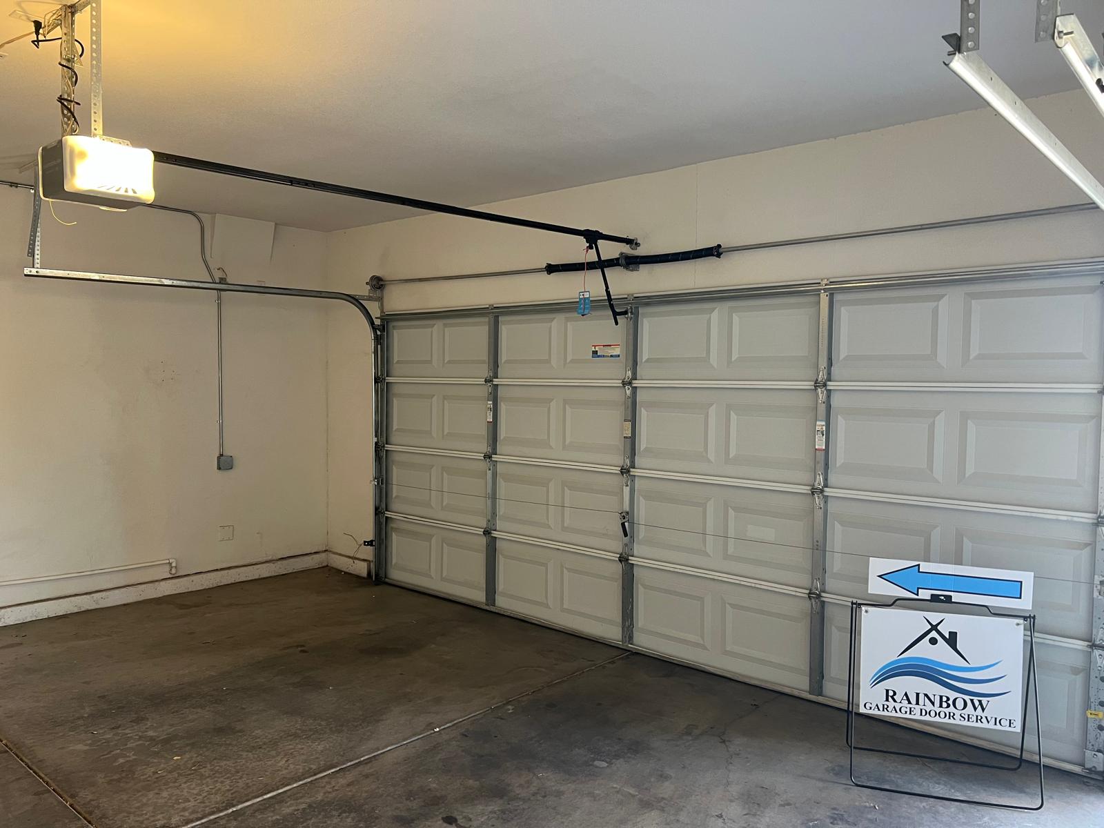 Clean installed white sectional garage door with opener and a Rainbow Garage Door A-frame sign